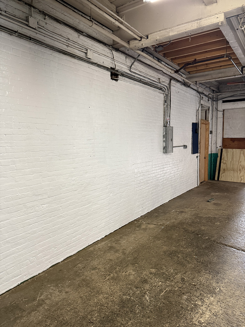 An empty white-painted brick room with exposed pipes and a concrete floor.